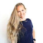 A woman with long blonde hair standing in front of a white wall